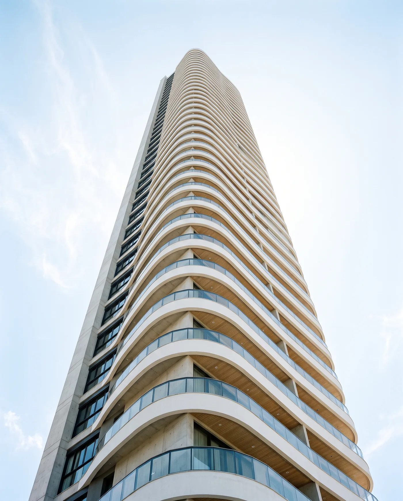 Torre residencial de alto padrão vista de baixo, varandas curvas em concreto branco e vidro